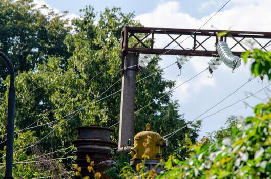 A power line pole with a large metal structure on top of it. The pole is surrounded by trees and bushes photo