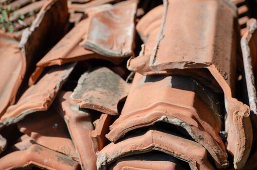 A pile of old, broken tiles. The tiles are in various sizes and shapes, and they are piled on top of each other. Concept of disarray and neglect, as the tiles have been discarded photo