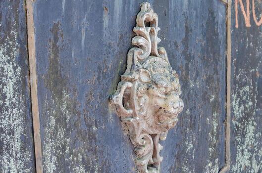 A stone lion head is on a wall. The lion head is carved and has a stone base. The lion head is on a wall that is covered in dirt and has graffiti on it photo