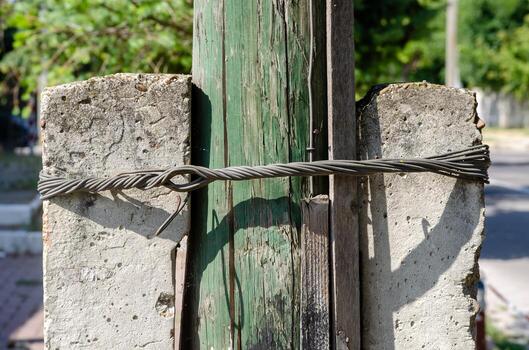A pole with a wire wrapped around it. The wire is attached to a cement block. The pole is green and the cement block is gray photo