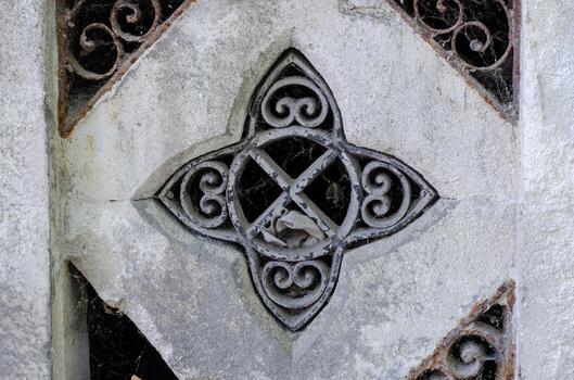 A stone carving of a cross with a spider web in the middle. The spider web is made of metal and is very detailed photo