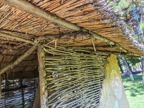 A hut made of wood and straw with a large, round design on the wall. The hut is located in a grassy area photo