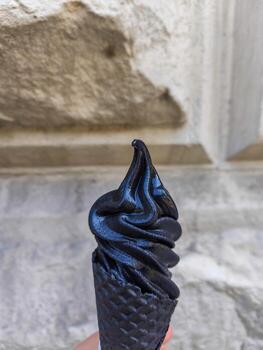 A person is holding a black ice cream cone. The cone is made of a wafer-like material and has a black frosting. Concept of indulgence and luxury photo