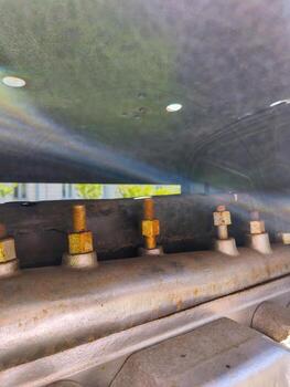 A close up of a car engine with a lot of bolts and screws. The bolts are yellow and the screws are silver. The engine is old and rusty photo