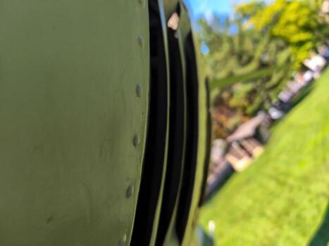 A close up of a green object with a black stripe. The object is a part of a machine or vehicle. The image has a calm and peaceful mood, as it is set in a grassy area with trees in the background photo