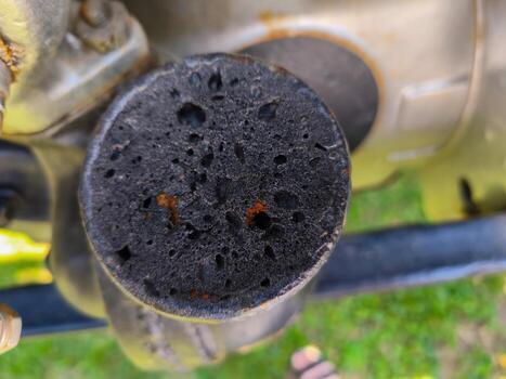 A black object with holes in it is sitting on a green grassy field. The object appears to be a piece of machinery, possibly a motorcycle, and it has been damaged. Concept of wear and tear photo