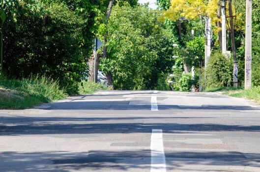 A road with a white line down the middle and trees in the background. The road is empty and there is no traffic photo