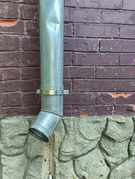 A metal pipe is attached to a building. The pipe is bent and has a metal cap on it photo