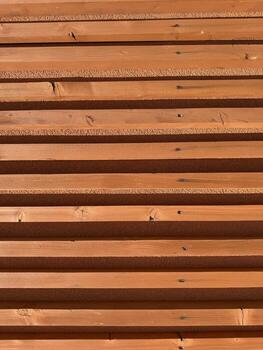 Symmetrical wooden slats in horizontal layout with terracotta tones texture and shadows architectural background modern building design surface structure geometry warm daylight pattern photo