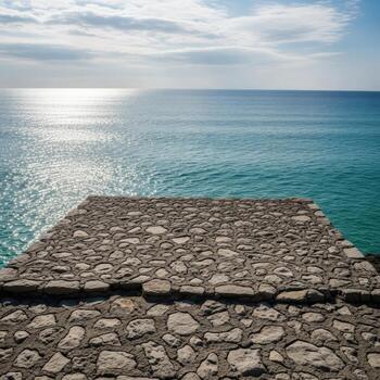 Stone walkway leading to the sparkling blue ocean under a cloudy sky photo