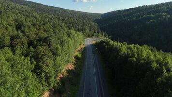 fuco aereo Visualizza di un vuoto montagna autostrada con un' acuto curva avvolgimento attraverso un' verde foresta valle su un' soleggiato giorno. video