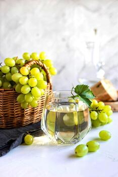 side view of white grape juice in glass with white grape in basket on white background photo