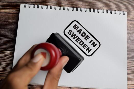 Red Handle Rubber Stamper and Made in Sweden text above book isolated on wooden background photo