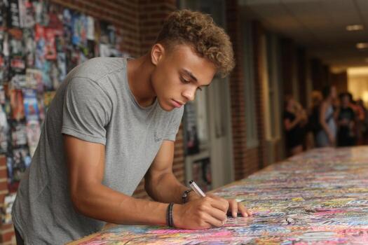 A young man signing on a table with colorful posters photo