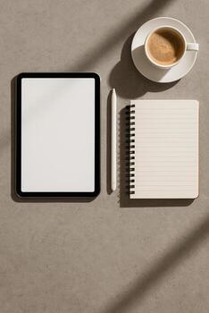 Digital tablet with blank screen, stylus and lined notebook with a cup of coffee on a stone desk. Warm sunlit shadows, clean minimal flat lay, top view, copy space. photo