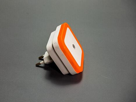 el imagen capturas un moderno, angular blanco y naranja Luz de noche en un gris superficie, sus pulcro diseño ofrecimiento un mezcla de funcionalidad y ambiente Encendiendo. foto