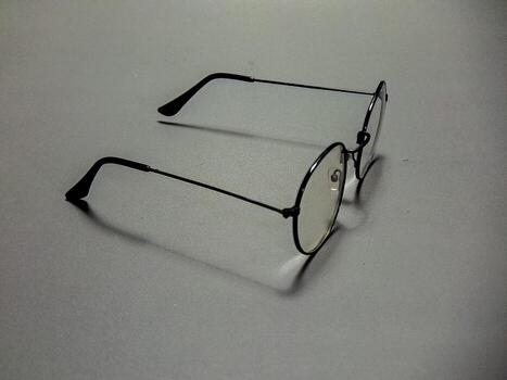 Eyeglasses with a thin black metal frame and round lenses rest on a gray surface, creating a minimalist, subtle and contemplative scene and a simple everyday style. photo