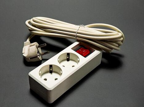 un blanco poder tira con dos salidas y enroscado cable se sienta en un gris superficie, el rojo cambiar es en indicando el fluir de electricidad, un común aparato para poder distribución. foto