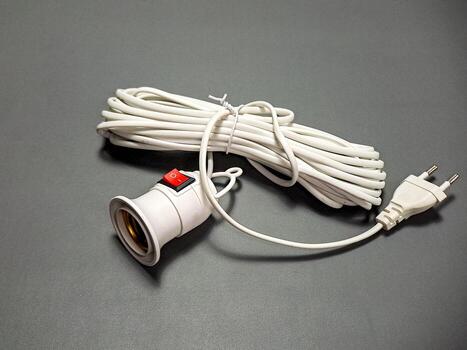 Arrangement of white electrical components includes a light bulb socket with red switch, cord neatly coiled and plug resting on a plain, muted gray surface. photo