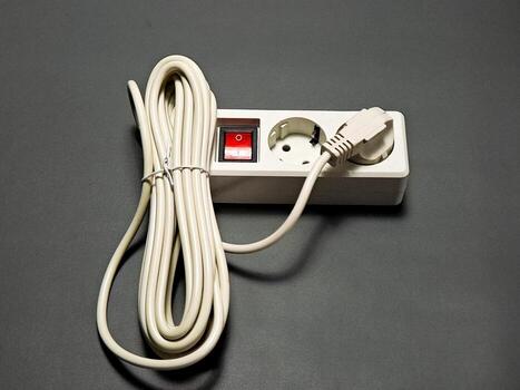 A coiled power cord is connected to a white power strip which has an on off switch, positioned on a plain dark gray surface,creating a practical and minimalistic scene photo