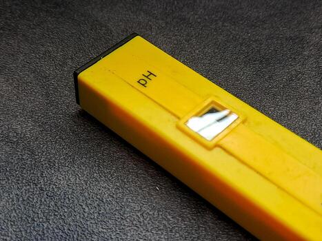 Isolated shot capturing a sleek, yellow pH meter displayed diagonally on a textured black surface, accentuating its design and function for soil or water quality testing. photo