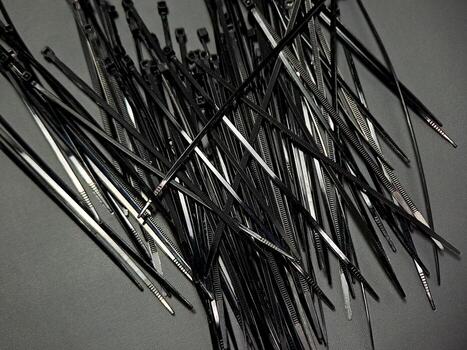 Organized chaos of numerous black zip ties scattered on a textured gray surface creating a dynamic and abstract composition emphasizing form, texture, and monochromatic color photo