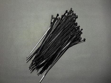 An organized array of black cable ties are presented on a neutral grey surface, showcasing the repetitive patterns and sleek design in a visually compelling manner. photo