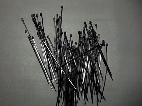 A jumble of flexible, black and silver nylon cable ties are scattered on a textured gray surface creating a sense of disarray and utility, showcasing order and control devices. photo