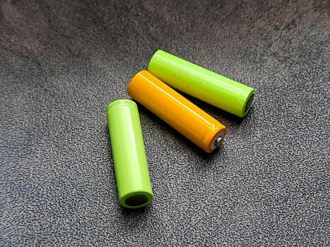 Energizing future An array of lithium-ion batteries, vibrant in green and orange, lay poised on a textured dark background, symbolizing portable power solutions for electronics. photo