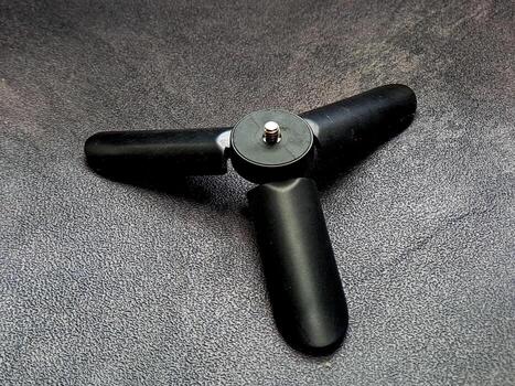 Captured is a sleek, three-legged black mini-tripod situated on a textured surface, demonstrating its simple design and functionality for supporting small devices on flat surfaces. photo