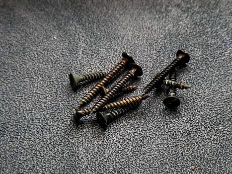 Arrangement of dark-toned metal screws with visible threads on a textured gray surface, creating a geometric composition that emphasizes lines and repeating forms. photo