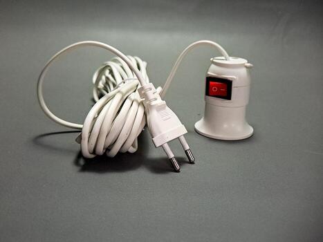 A coiled white power cord with a European plug and a socket with a red switch sits on a gray surface, creating a still life of modern electrical components, simple and functional. photo
