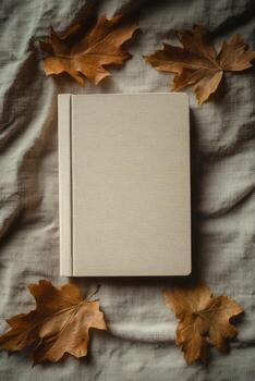 Beige textured notebook rests centered on fabric surrounded by autumn leaves forming a simple display photo