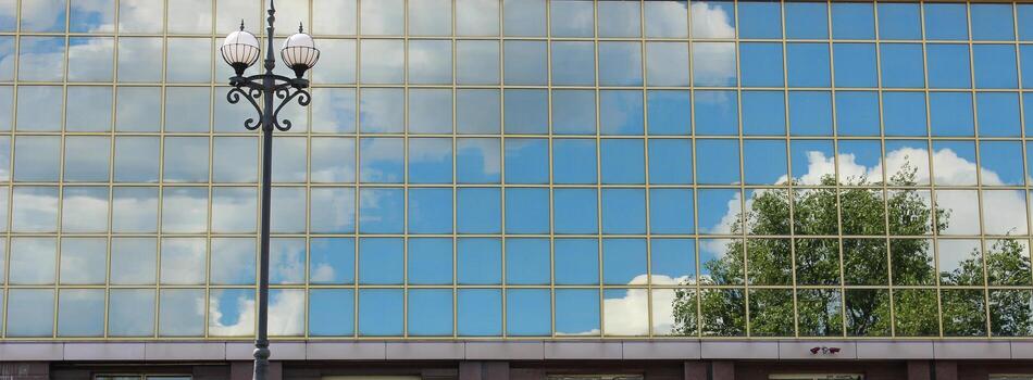 Reflection Of Trees, Sky And Clouds In Glass Facade Of Modern Building With Street Lamp In Front photo