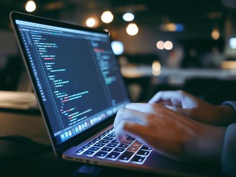 Close-up of a person coding on a laptop in a dimly lit workspace, creating a focused atmosphere. photo