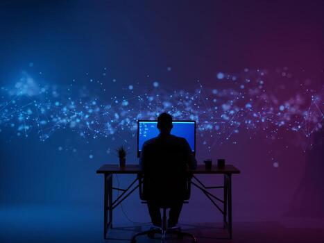 Silhouette of a man working at a computer with abstract digital lights in the background. photo