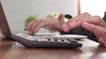en händer engagerad i arbete använder sig av en kalkylator och bärbar dator på en skrivbord. representerar kontor uppgifter, bokföring, eller finansiell analys i en professionell miljö. video