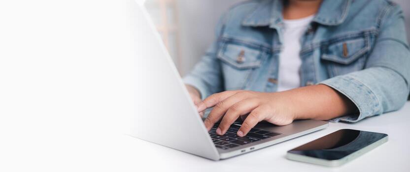 Person typing on laptop with smartphone placed on desk, copy space on left, symbolizing remote work, digital communication, and the use of technology in a modern professional workspace photo