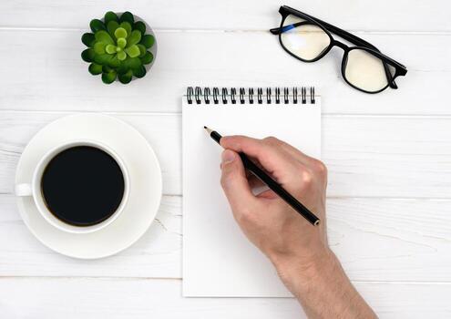 Man's hand makes notes in an empty notebook. Working table. Workplace. Top view. Flatlay. Selective focus. photo