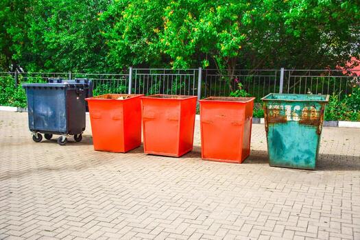 Trash bins in the streen. Colorful trash bins are lined up on a paved area, emphasizing their varying conditions and the need for effective waste management and recycling in urban environments. photo