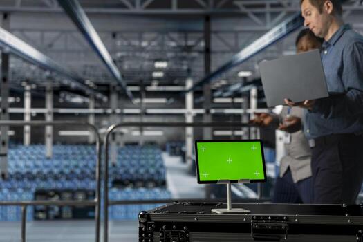 Server room colleagues managing large scale IT infrastructure using mockup device. Close up of green screen tablet in front of data center admins coordinating deployment of new server architectures photo