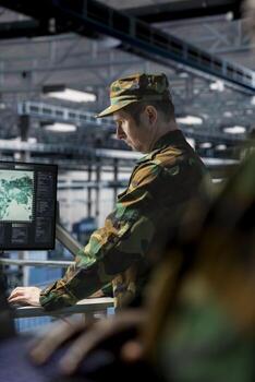 Soldier in server hub checking reports at data operations workstation monitor. Army information expert wearing uniform monitoring systems using display in operational data center photo