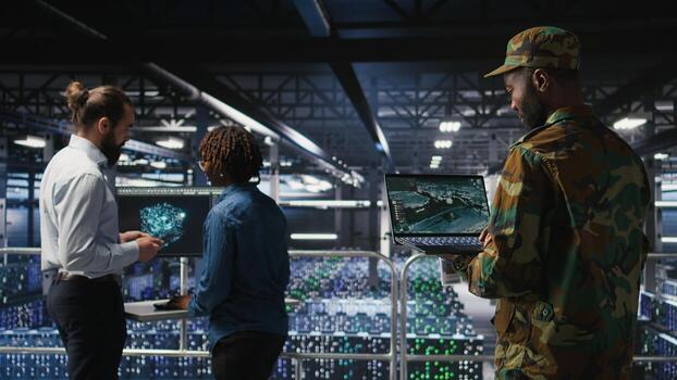 Military technician in data center monitoring warfare drone telemetry on laptop dashboard. IT specialist in army server room using tactical interface on notebook to support aerial operations photo