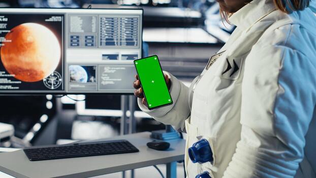 Astronaut using green screen smartphone to text friends before landing spaceship on Mars. Woman using chroma key phone to chat with family during mission to red planet surface in deep space photo