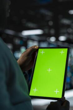 Close up of software developer in data center using green screen tablet to check for server performance issues. Server hub worker fixing malfunctions slowing down hardware using mockup device photo