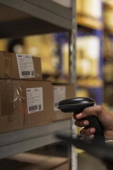 Close up of industrial depot worker scanning parcel details using tracking software, walking near huge storage racks. E-commerce delivery management system ensures accuracy in order processing. photo