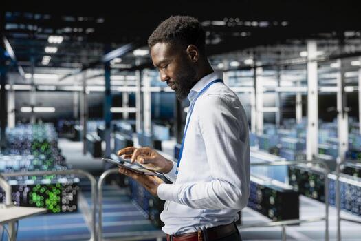 African american server hub worker checking code on tablet, reviewing AI LLM visualization on elevated industrial platform. Technician monitoring artificial intelligence systems infrastructure. photo