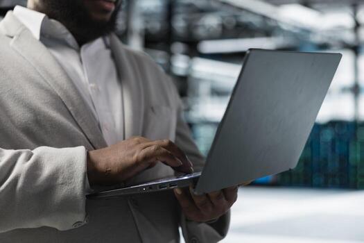 Close up of data center worker running error checking utilities on laptop, automating anomaly detection. Server farm employee monitoring infrastructure performance, looking for network issues photo