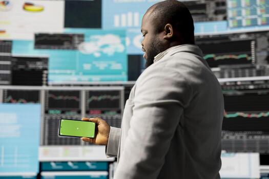 African american administrator uses copy space on phone and examines dashboards, ensuring analytics and performance metrics with KPI projections. Management decision for innovation. photo