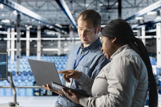 Team of data center admins using laptop to manage software updates for system stability. Teamworking server room IT specialists optimizing performance with device, configuring infrastructure photo